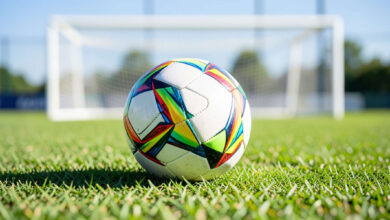 Pallone da calcio sull'erba di un campo, con la porta sullo sfondo (immagine generata con IA)
